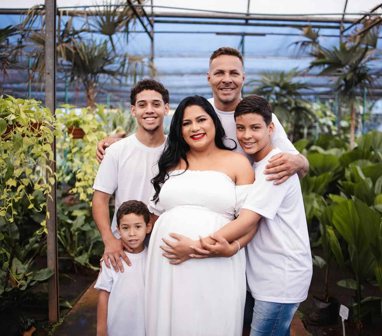 A family poses for a maternity photo in a greenhouse